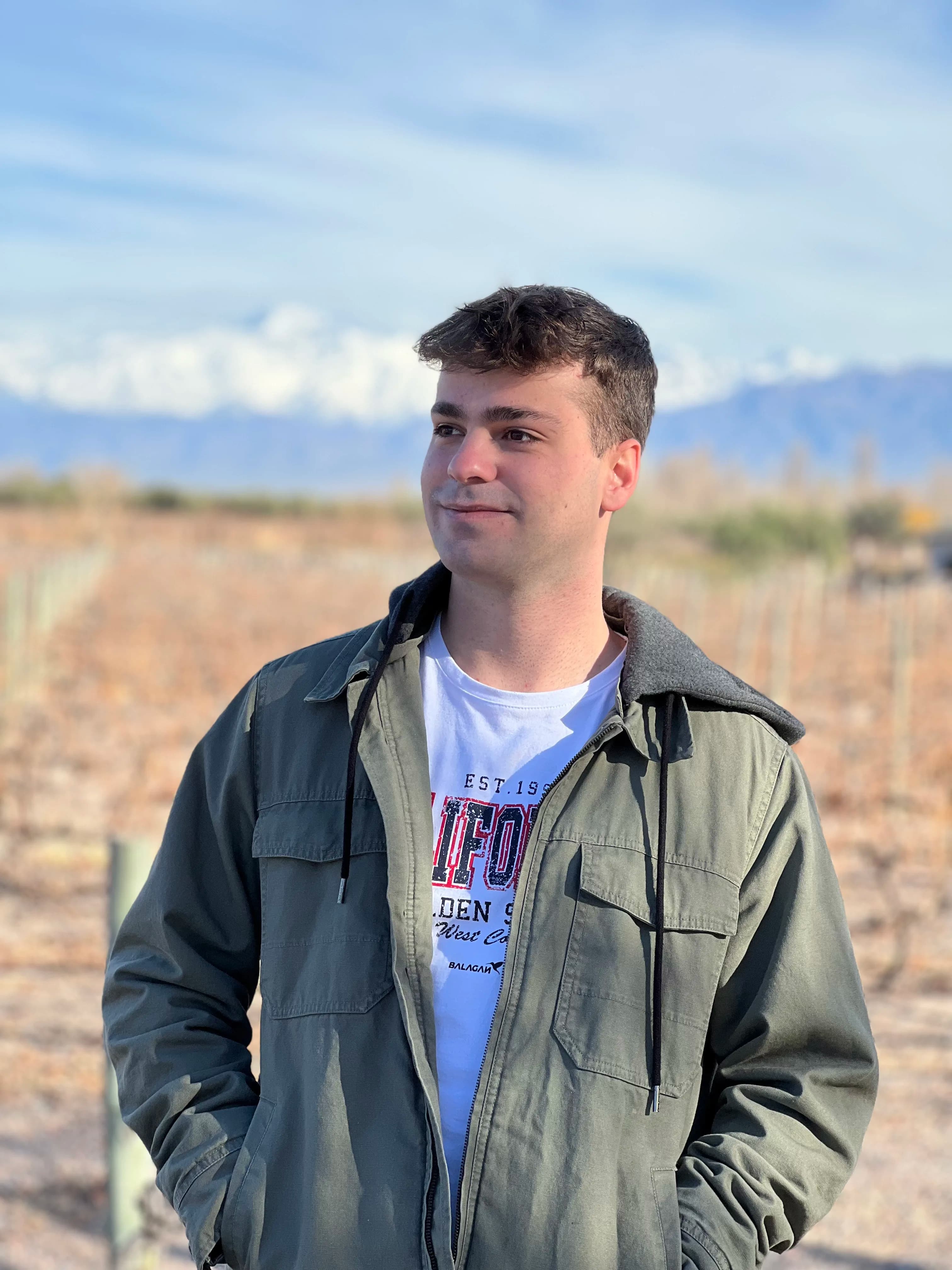Retrato de Federico Villagra al aire libre, con chaqueta verde y un paisaje de fondo.
