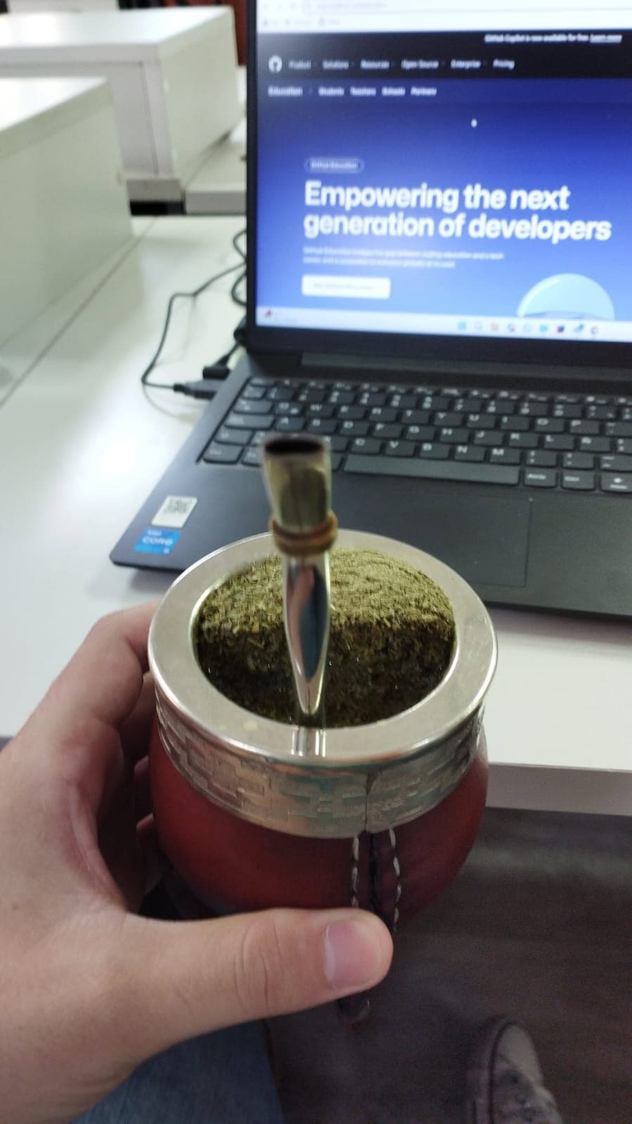 Una mano sosteniendo un mate junto a un portátil.